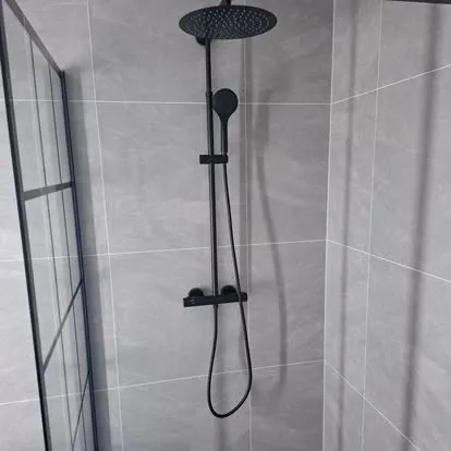 Sort takdusj på grå flisvegg bak en glassvegg